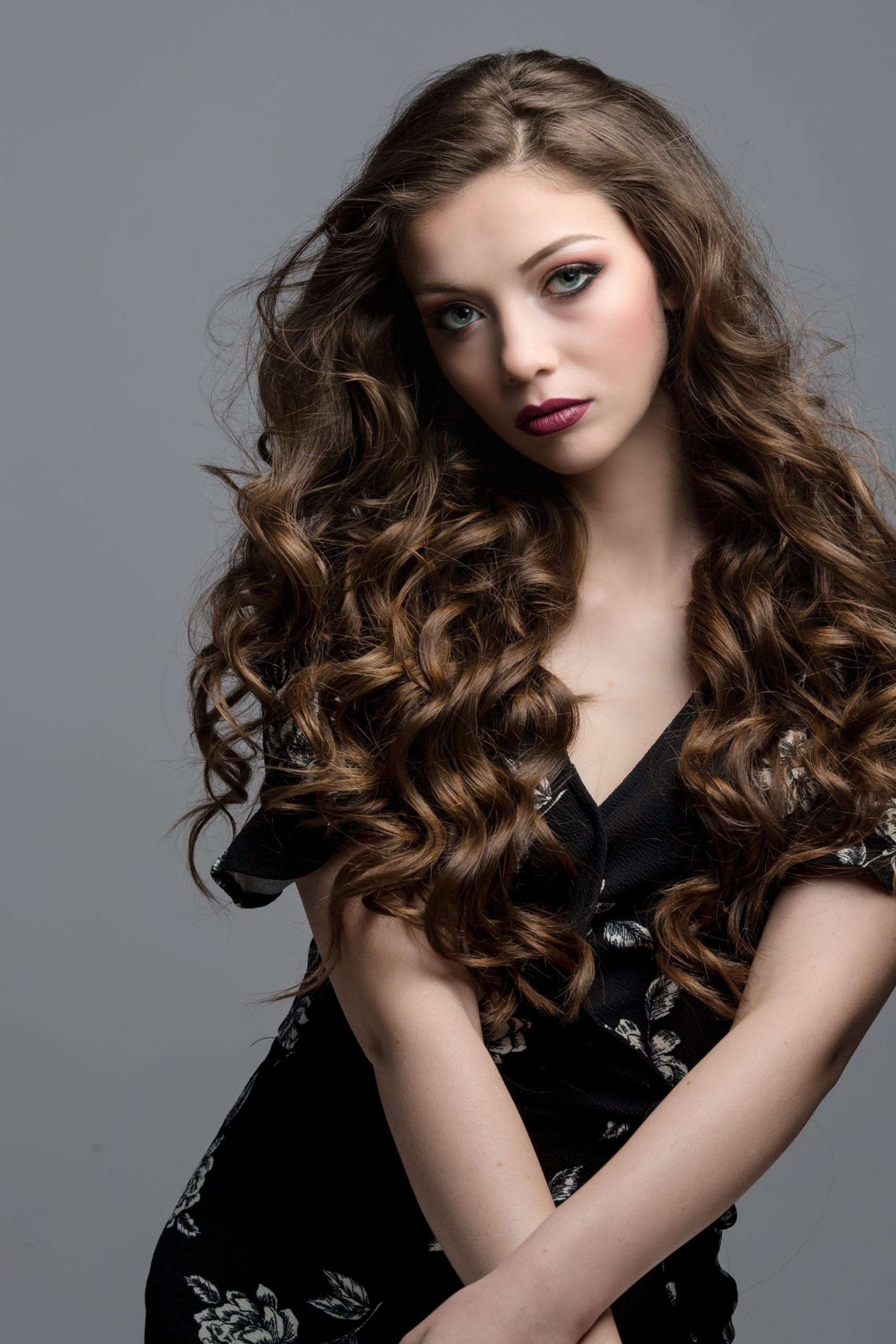 Woman with long, wavy brown hair, wearing a black dress, looking at the camera.