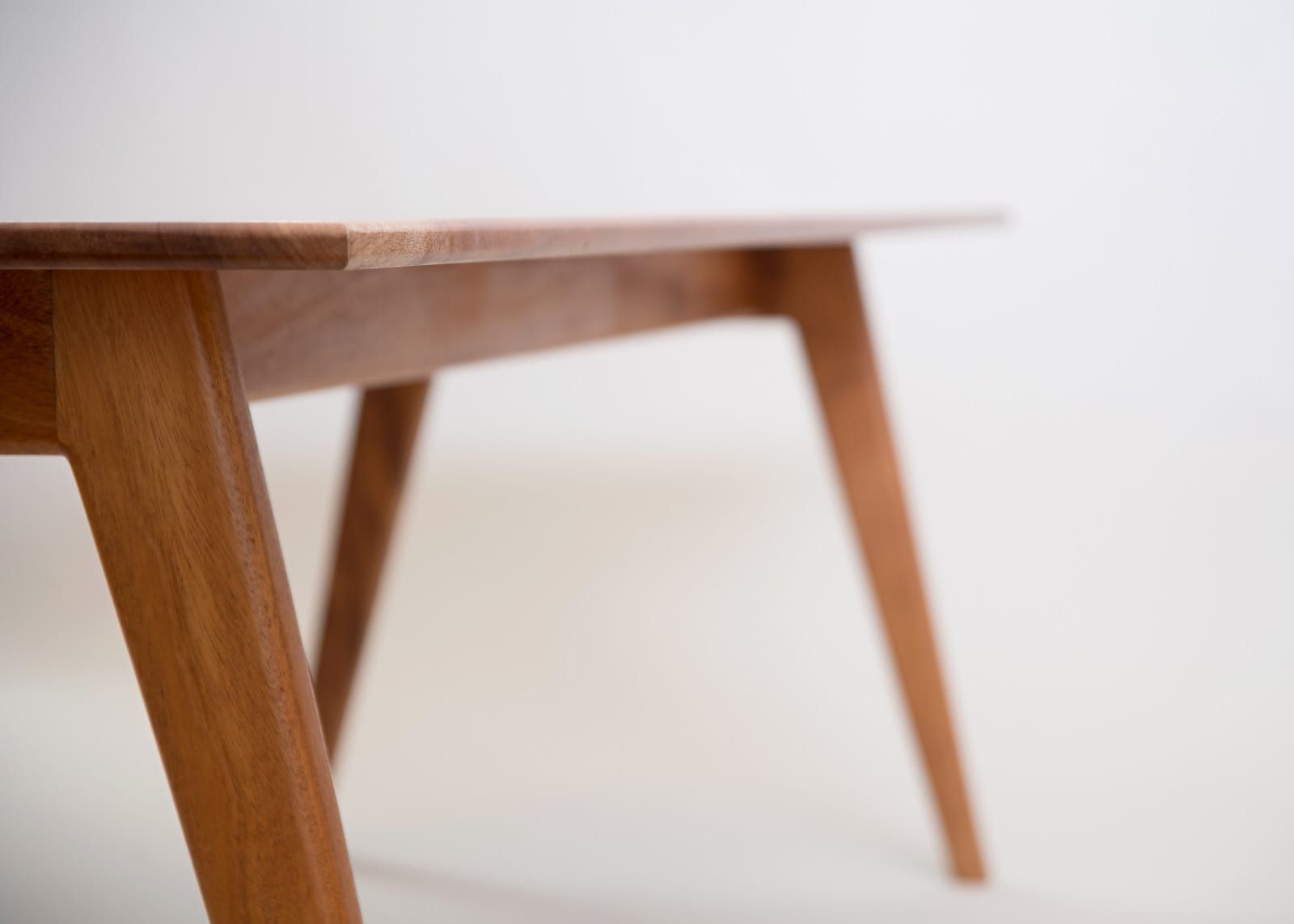 Wooden table with angled legs, light brown, against a white background.
