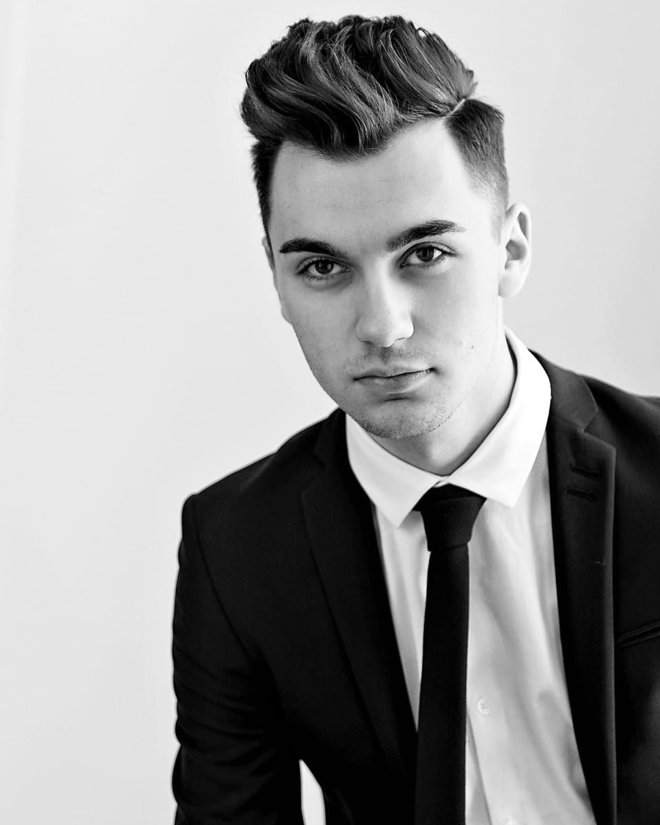 Man in suit and tie with slicked-back hair, looking directly at the camera.