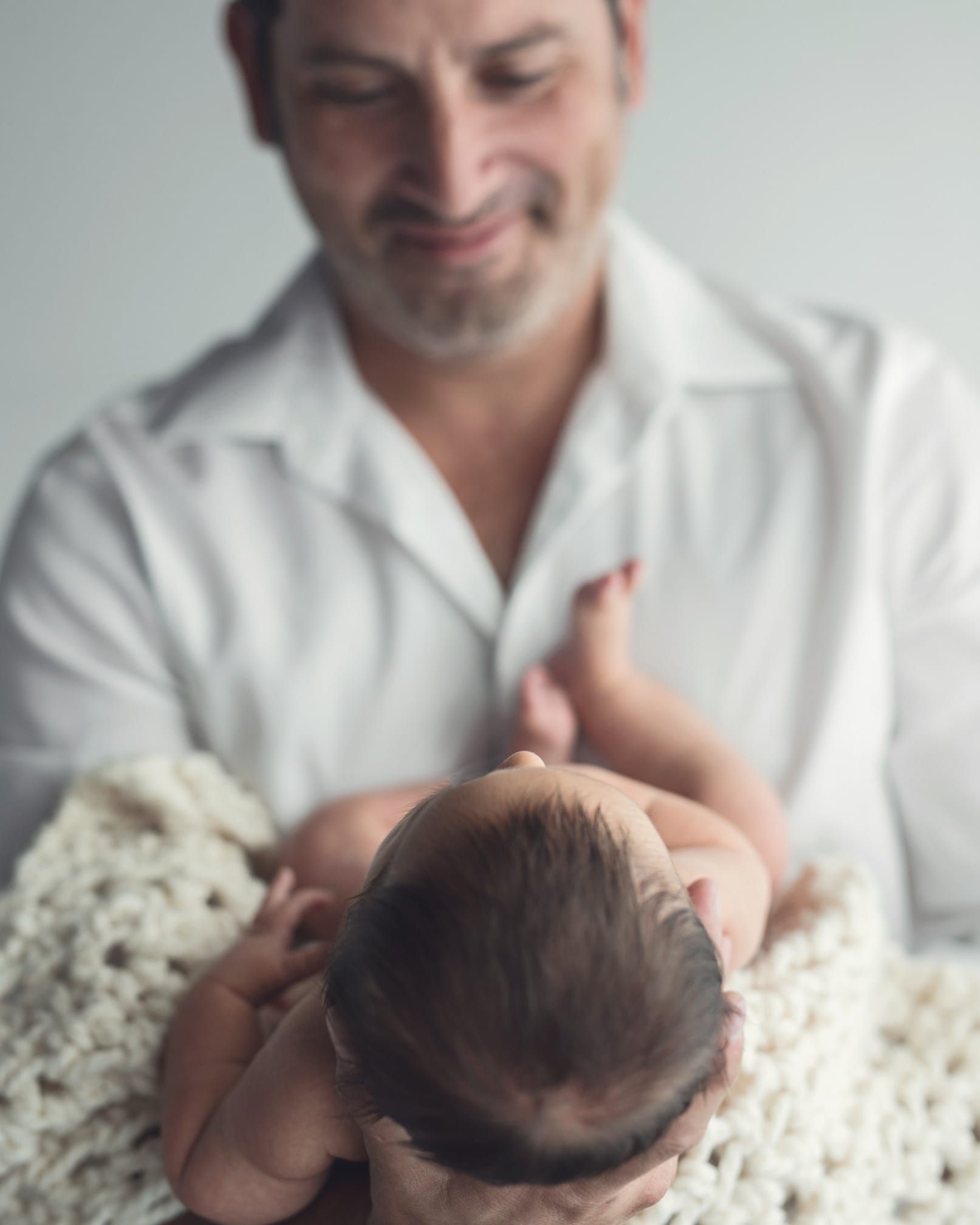 Father gazing adoringly at newborn baby lying in a blanket.