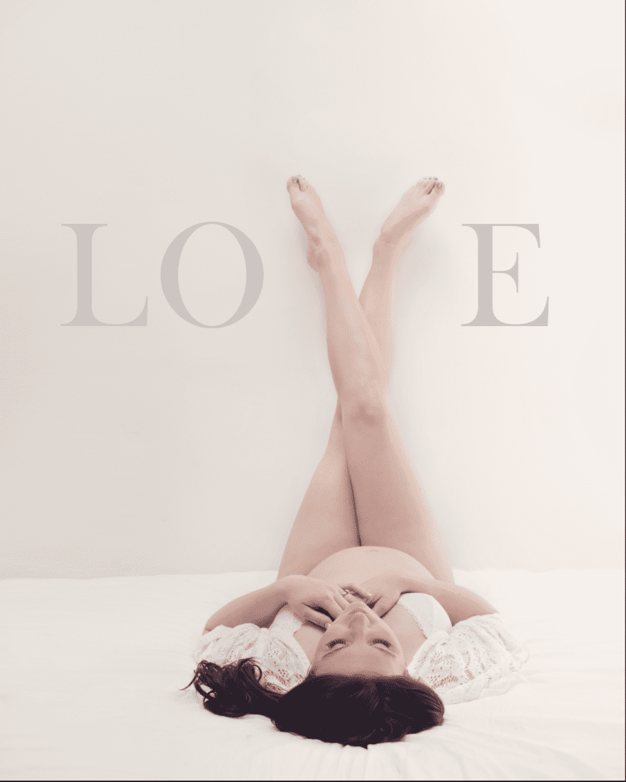 Pregnant woman lying on a bed, legs crossed up the wall, arms over chest, with 