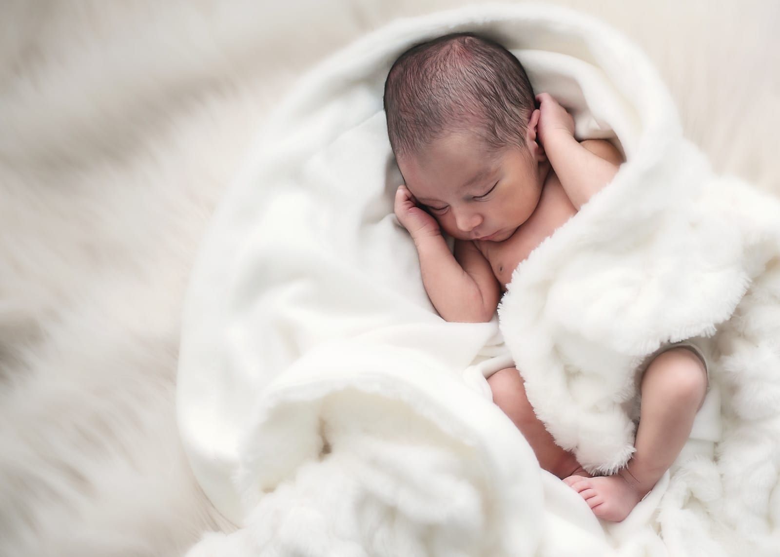 Newborn baby sleeping, wrapped in a fluffy white blanket, peaceful expression.