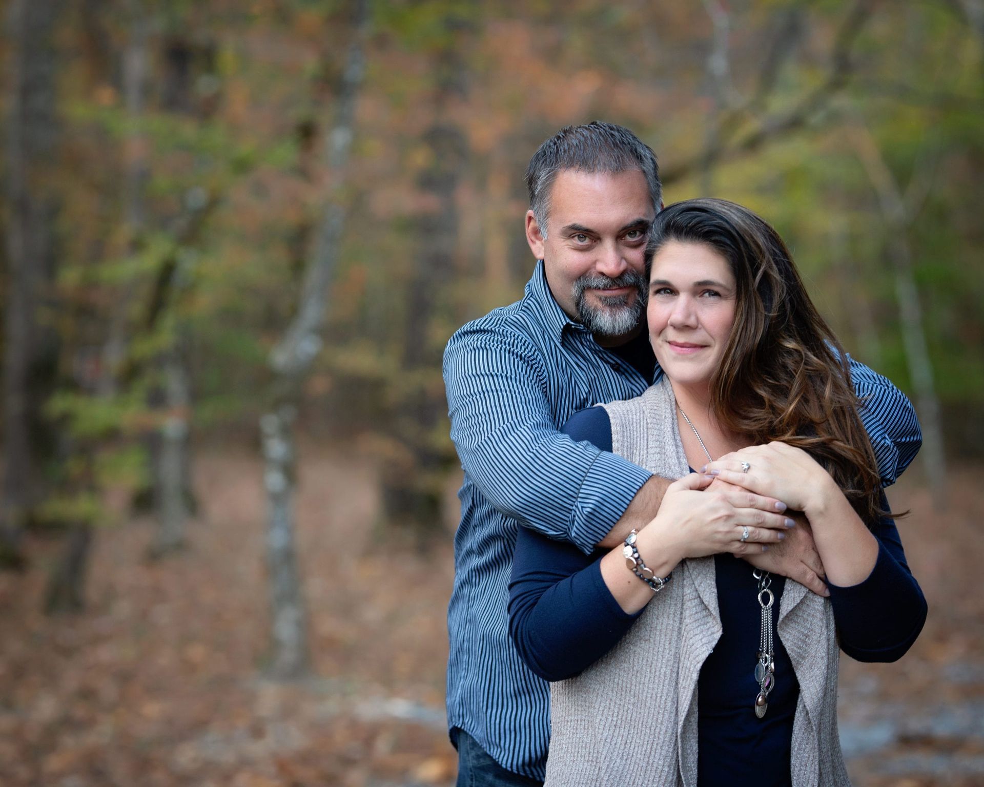 Man embracing woman outdoors, fall foliage backdrop. They smile.