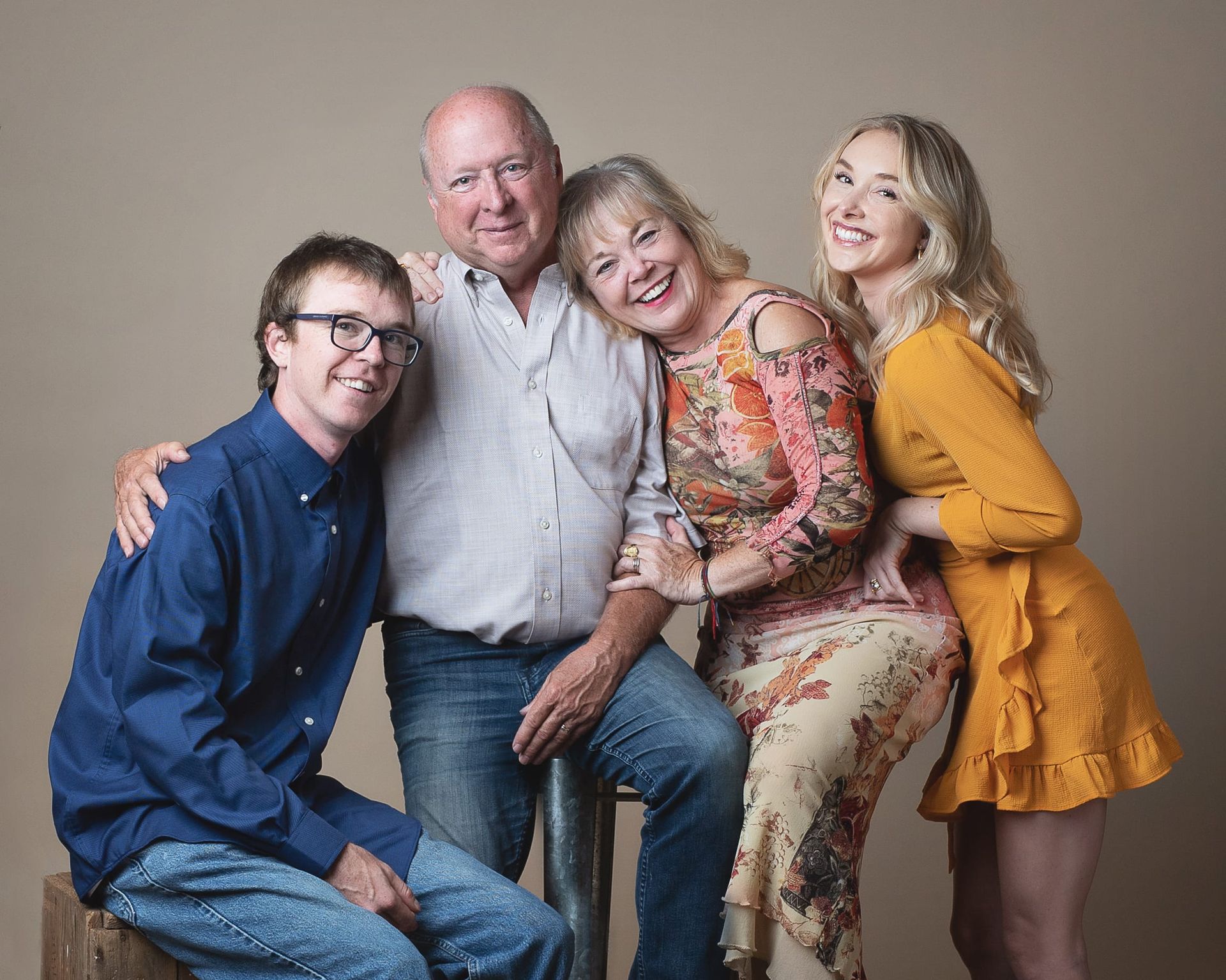 Family of four posing indoors smiling; man with arm around woman, daughter beside.