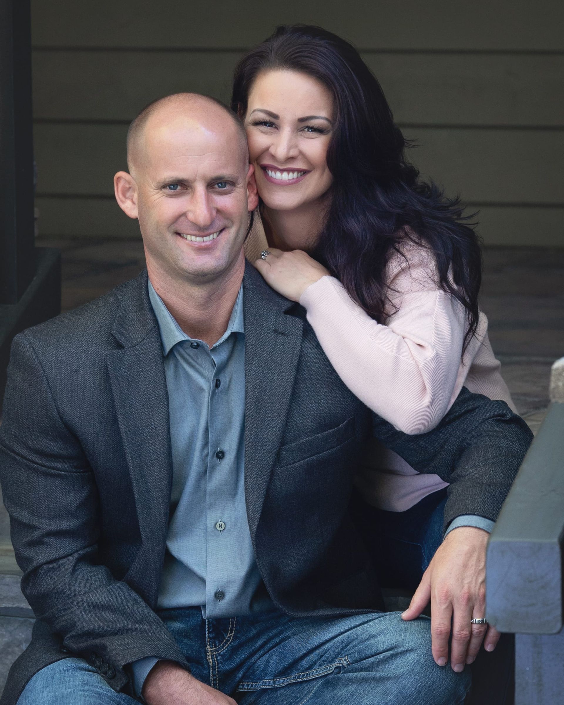 Man and woman smiling, seated on steps; woman's arm around man's shoulder.