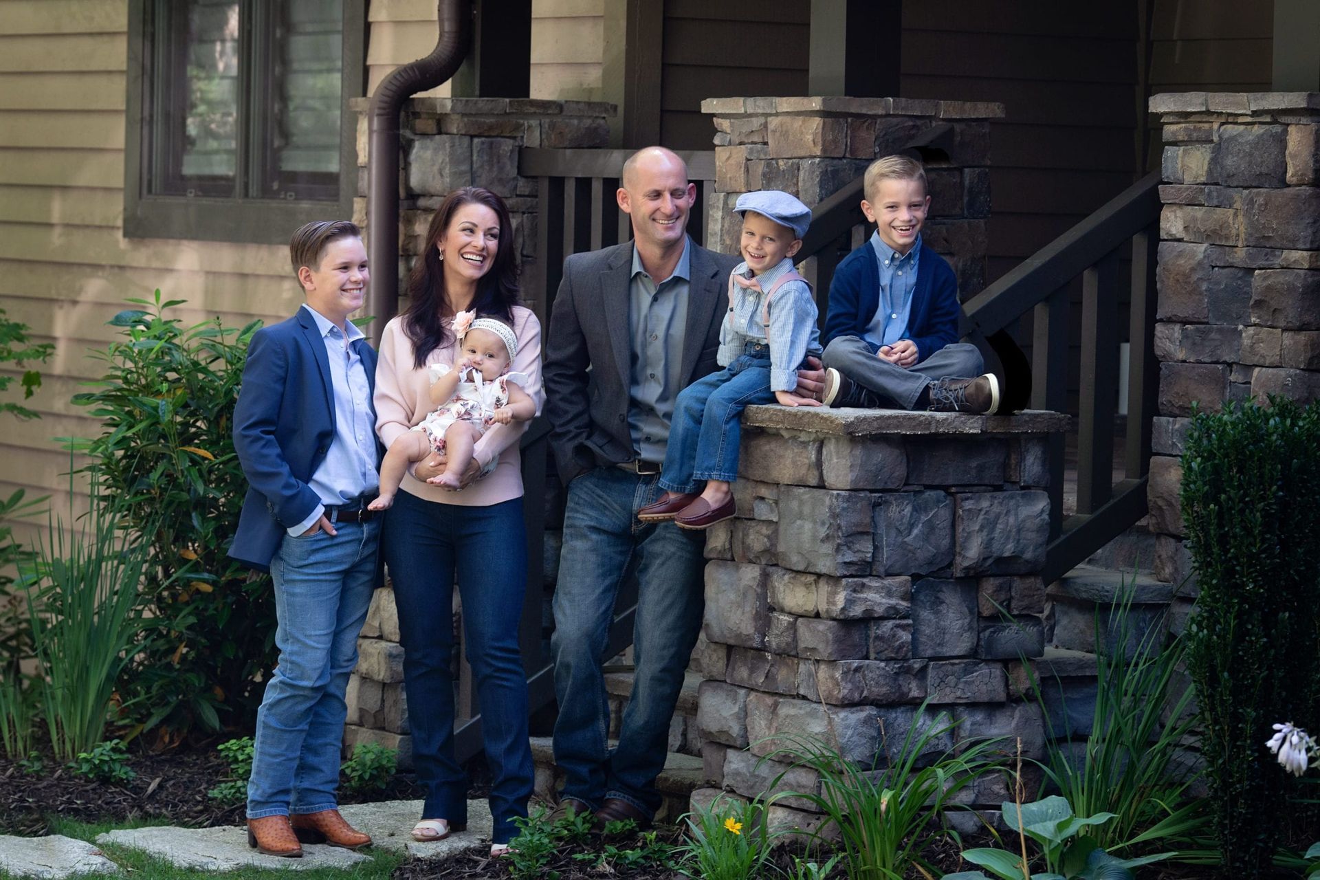 Family of six poses outside their home: two boys, baby, parents.