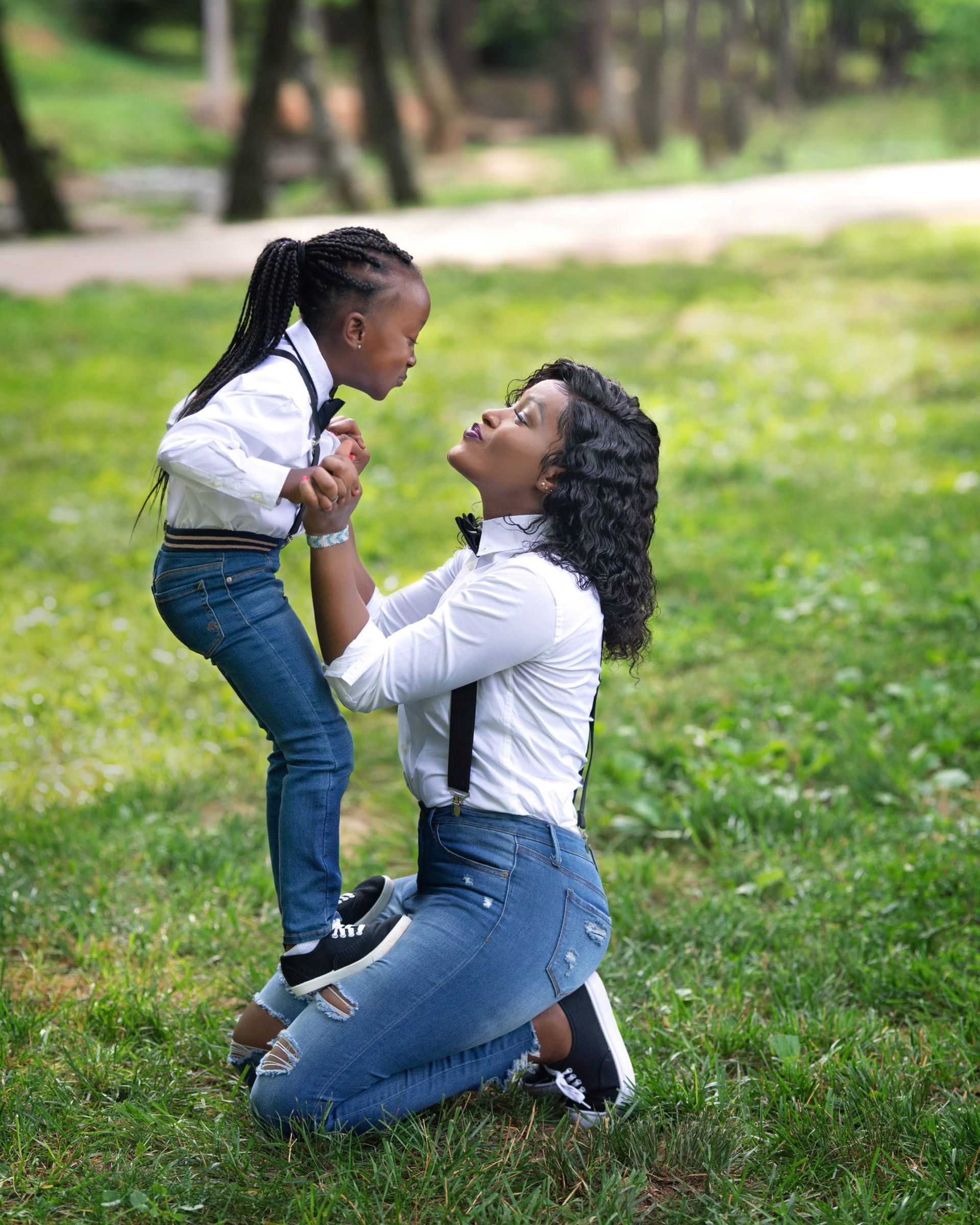 Mother and daughter in matching outfits, holding hands in a park, about to kiss.