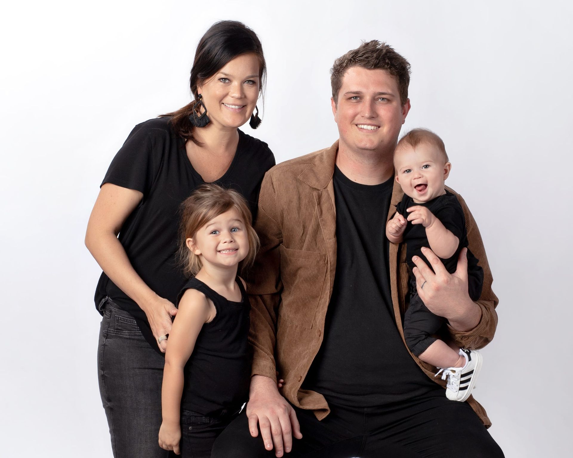 Family of four posing, smiling. Mother, father, daughter, baby. Neutral background.
