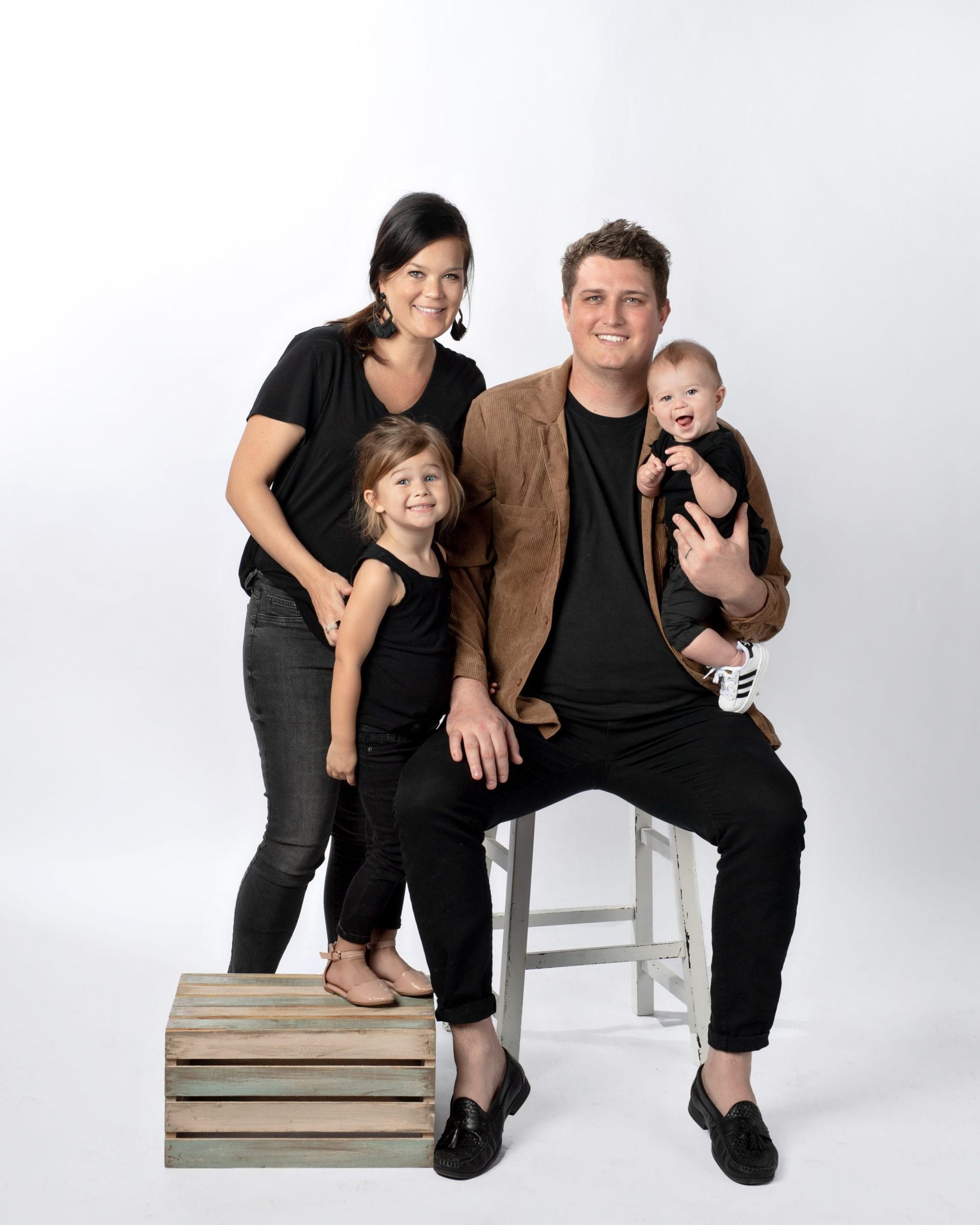 Family of four in black outfits, posing against a white background.