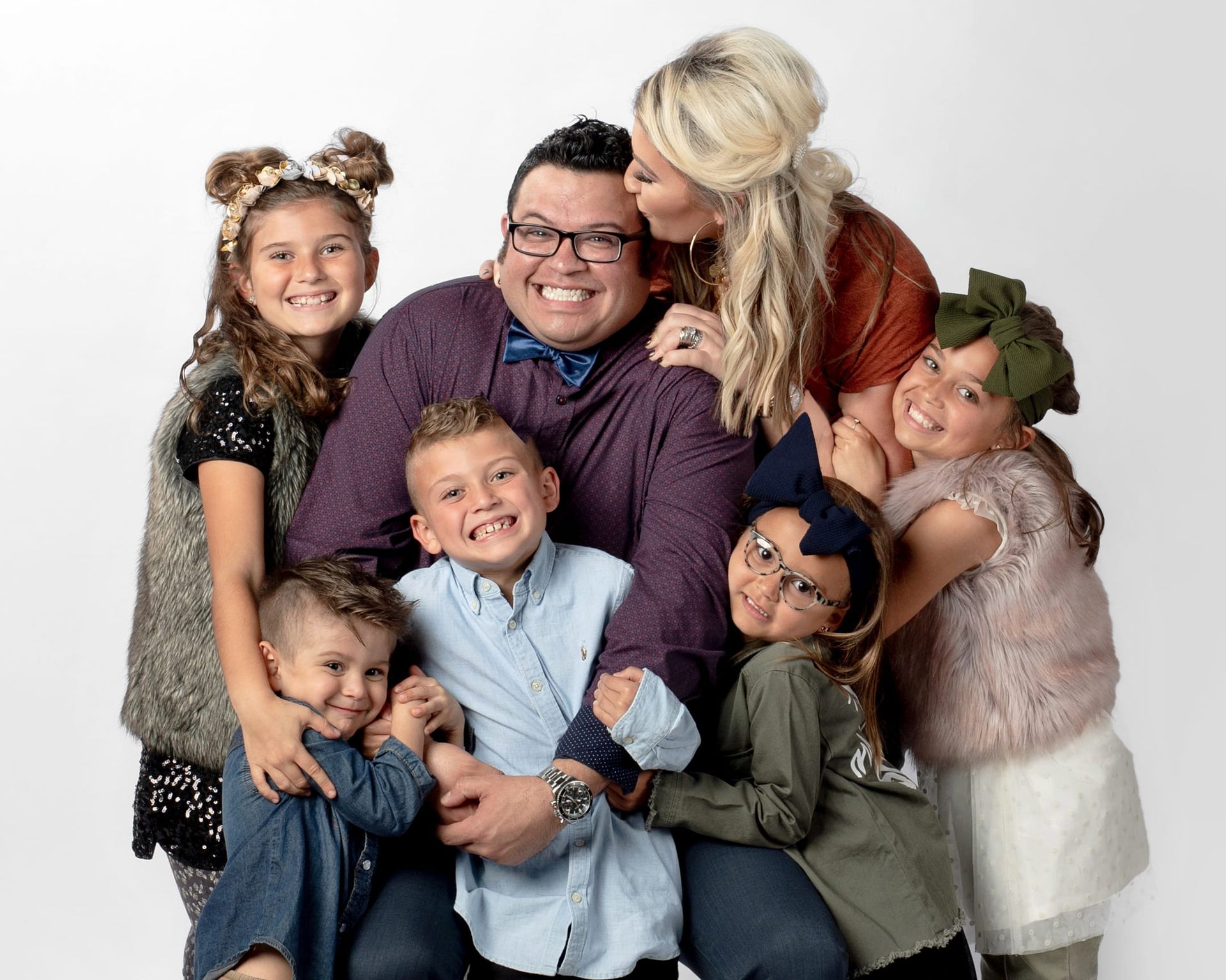 Family portrait: father surrounded by six children; mother kisses father's cheek.