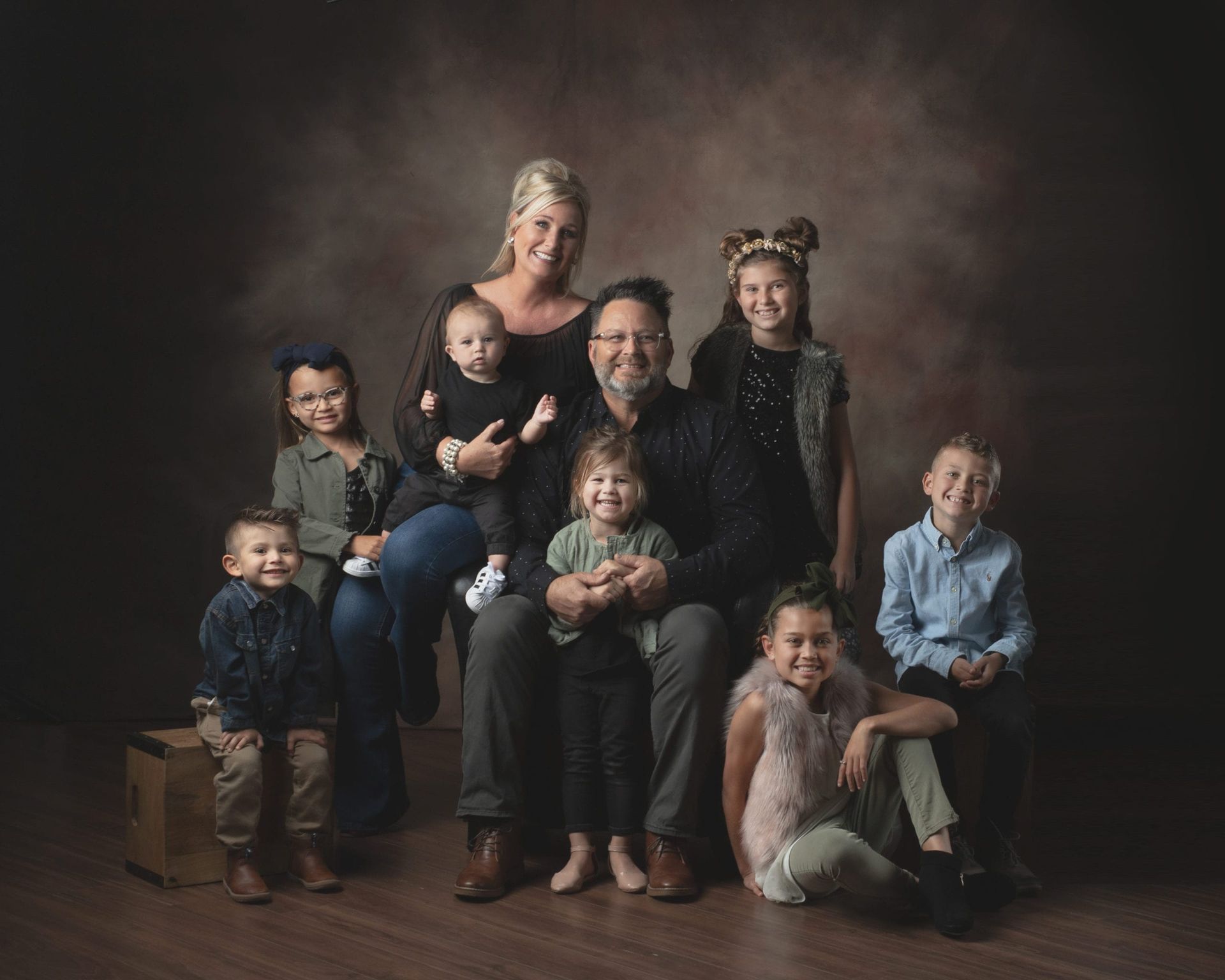 Family portrait: parents seated, surrounded by eight children, studio setting, warm tones.