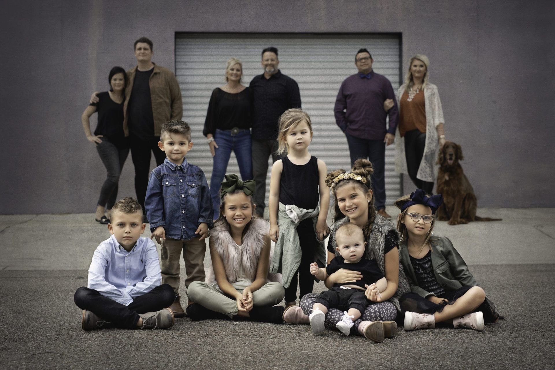 Family portrait posing outdoors in front of a grey garage door. People of varying ages are in dark clothing.