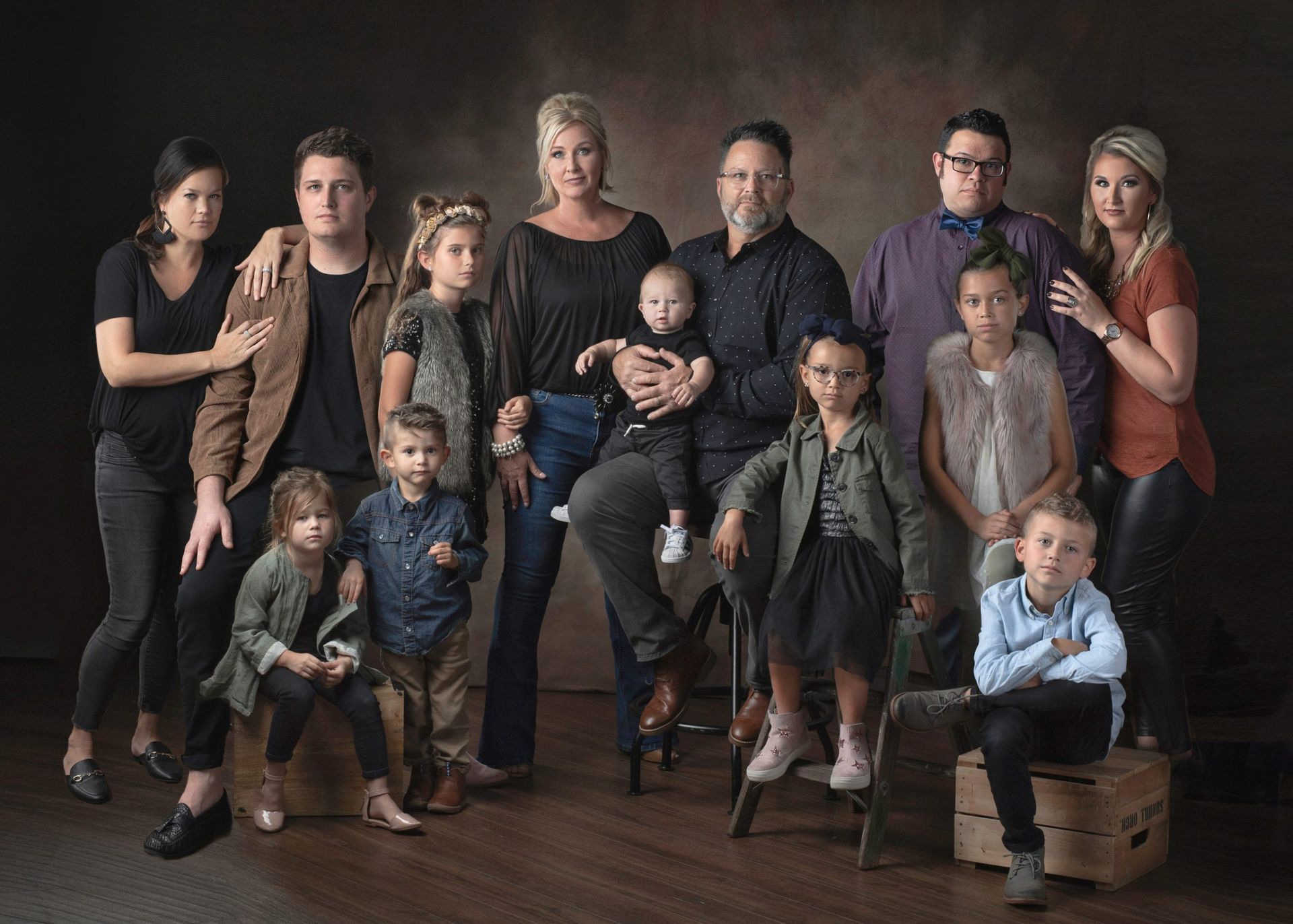 Large family portrait, posing in studio. Brown background, diverse group; adults & children.