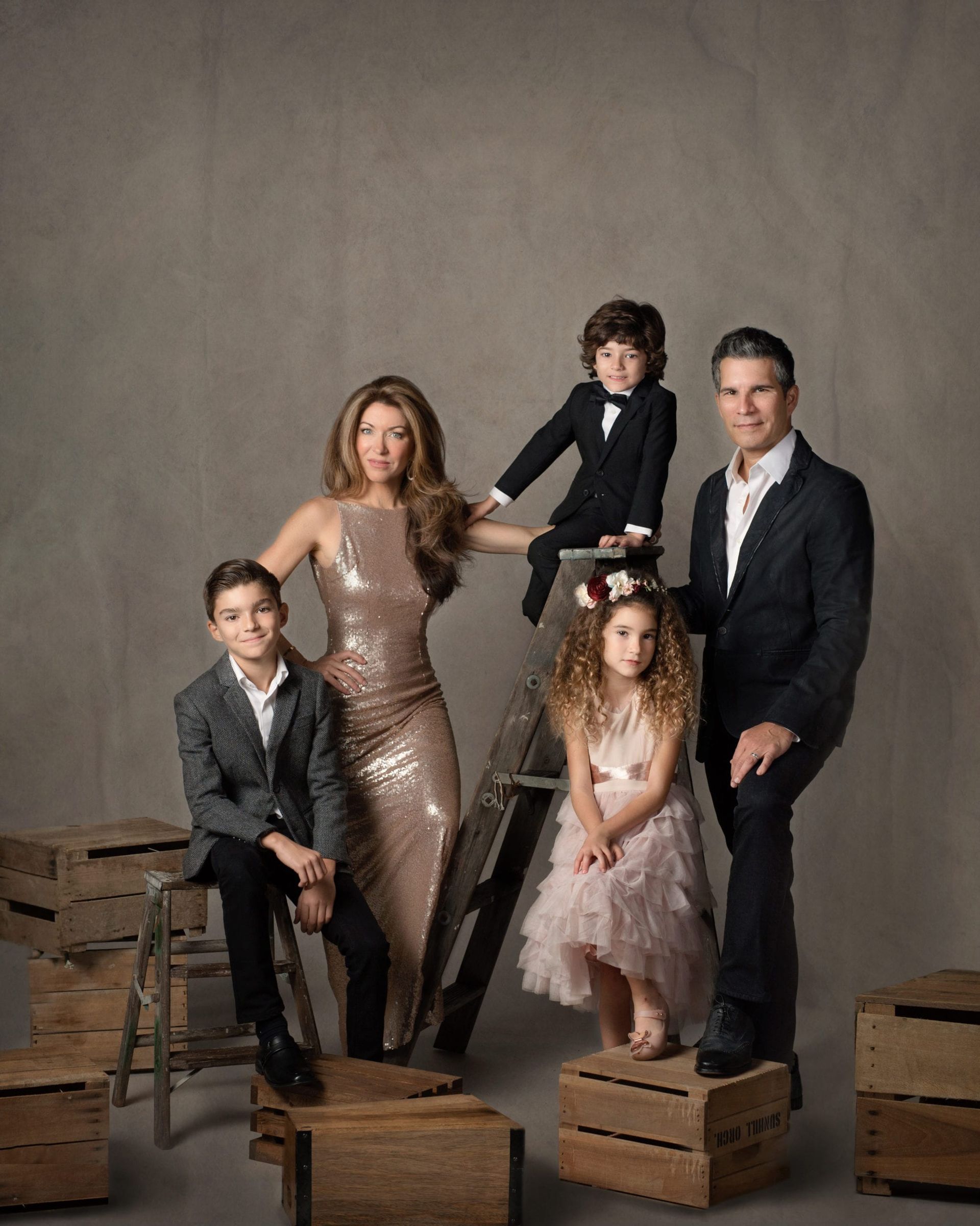 Family portrait: mother in gold dress, father in suit, three children pose on crates.