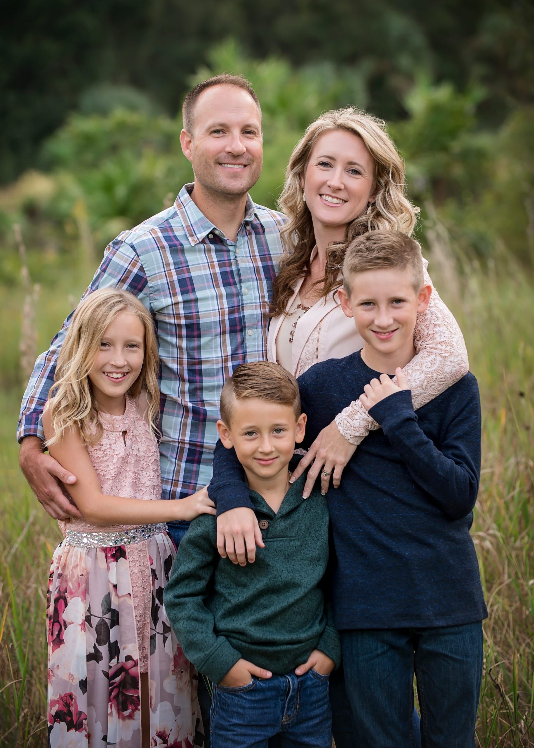 Family of five smiling, posing in a grassy field; parents with three children.