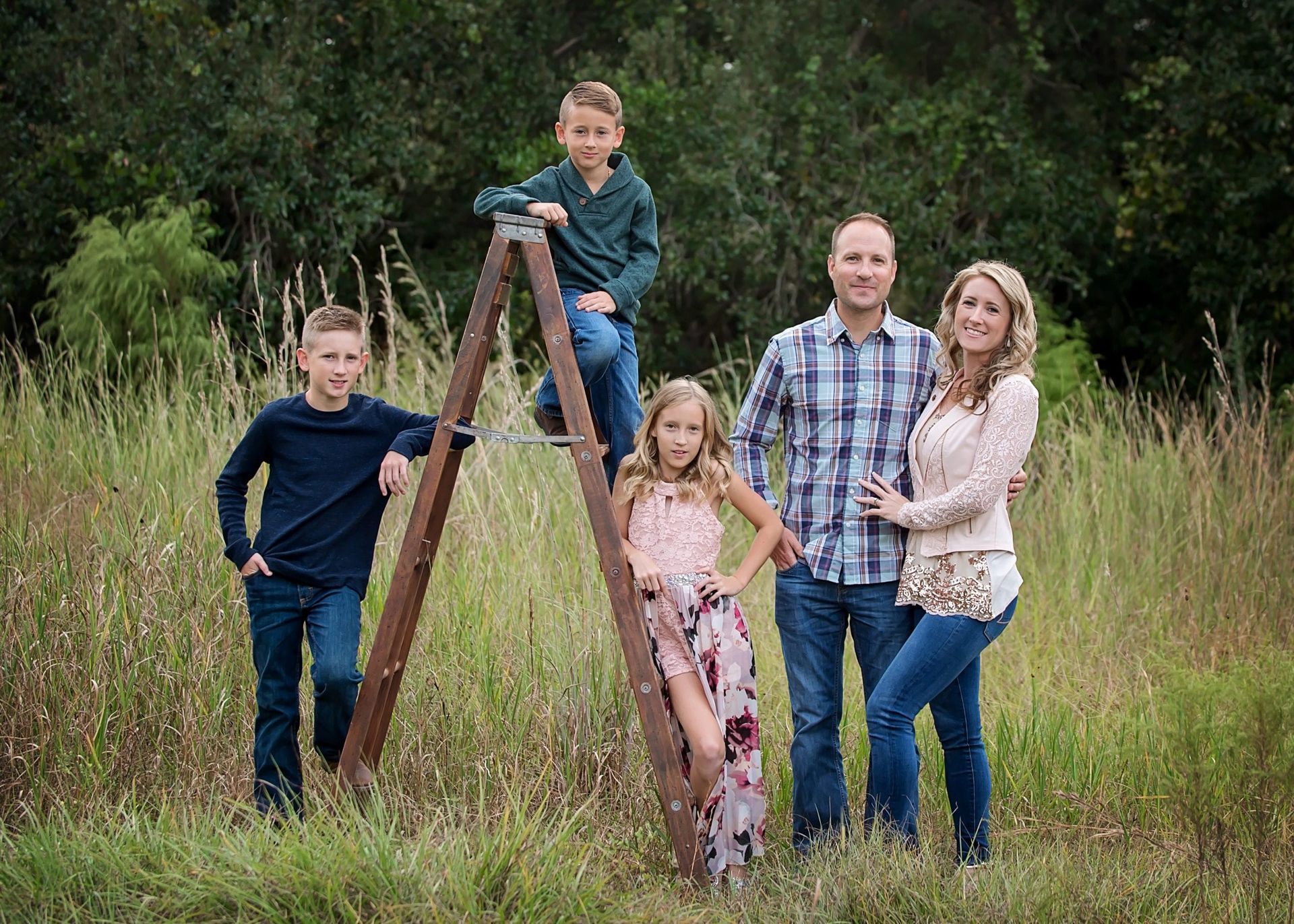 Family of five posing outdoors; two boys on a ladder, daughter on the ladder, parents smiling.
