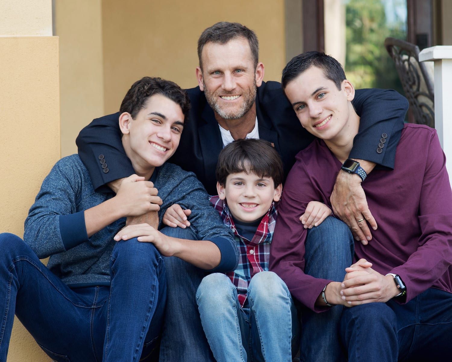 Father with three sons smiling outdoors, arms around each other.