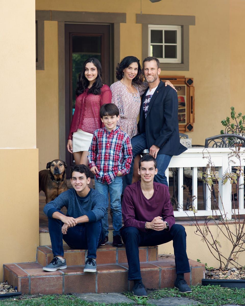 Family of six poses on porch steps. Woman, man, and four children; dog sits nearby.