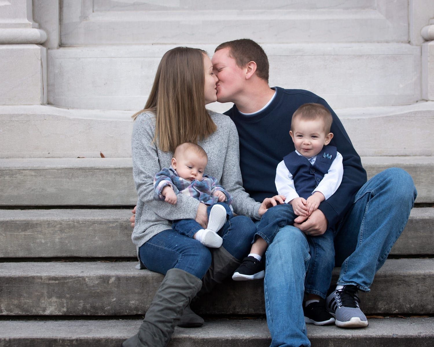 Family of four on steps: parents kissing, holding babies.