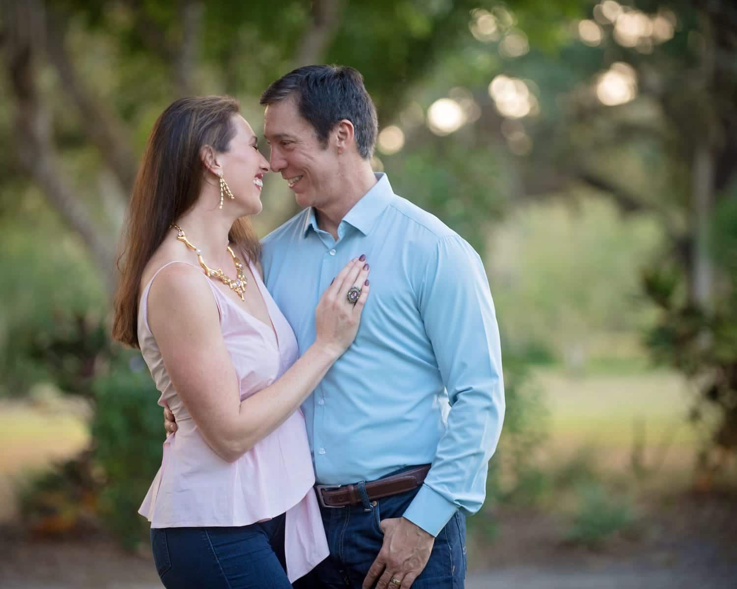 Couple embracing outdoors, woman in pink top, man in blue shirt, smiling at each other.
