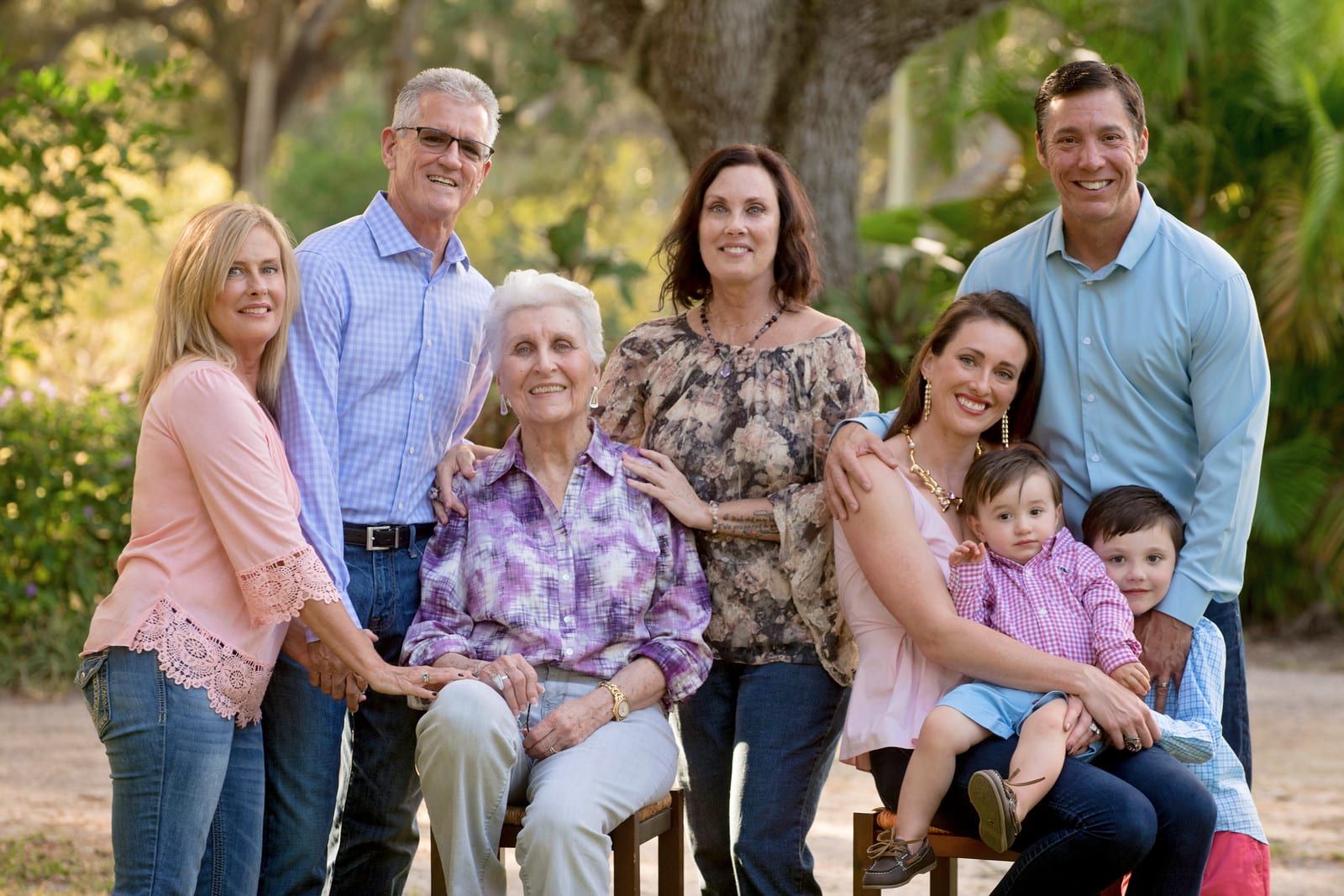 Family group outdoors, smiling at camera. Elderly woman seated, surrounded by adults and children.