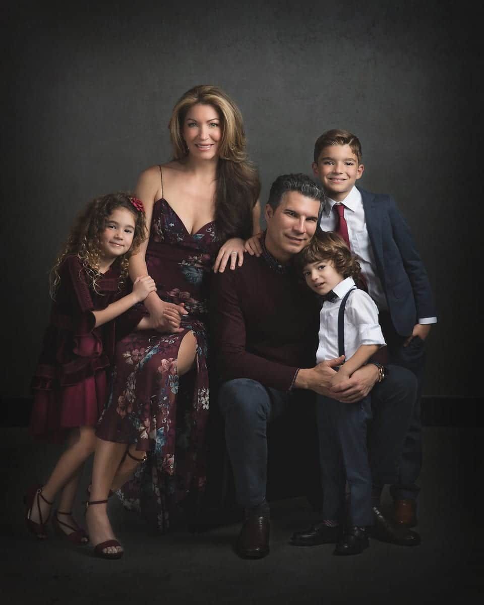 Family portrait: mother, father, three children, posed; formal attire, smiles, dark background.