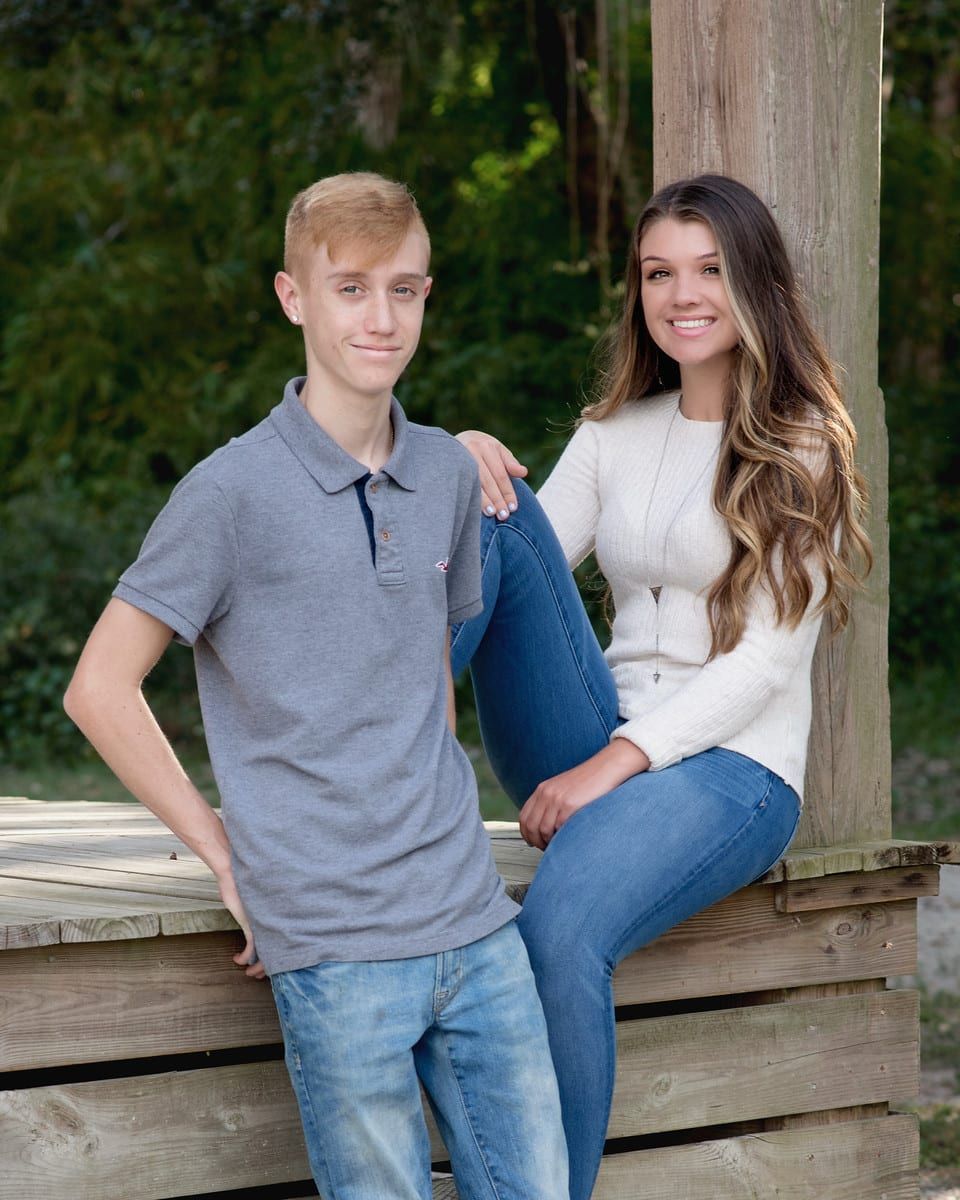 Teen boy and girl smiling, posing outdoors. Boy wears polo shirt, girl sweater.