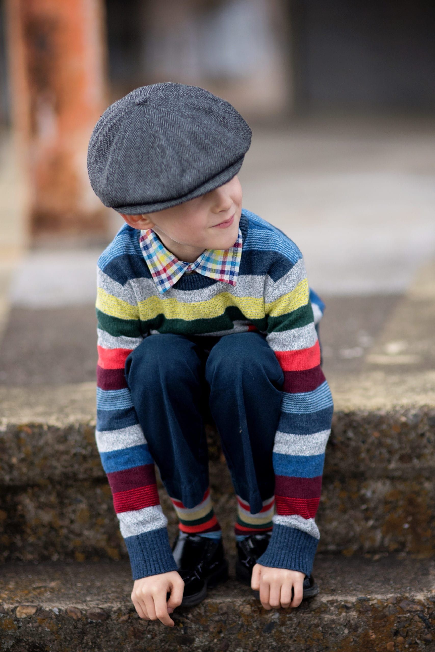 Boy in cap and striped sweater, sitting on steps, looking to the side.