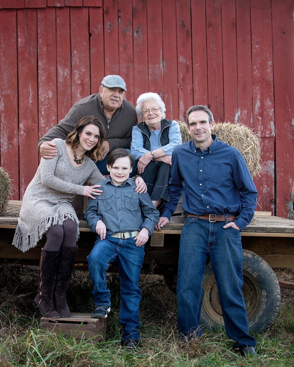 Family posing in front of a red barn; two women, three men, and a young boy.