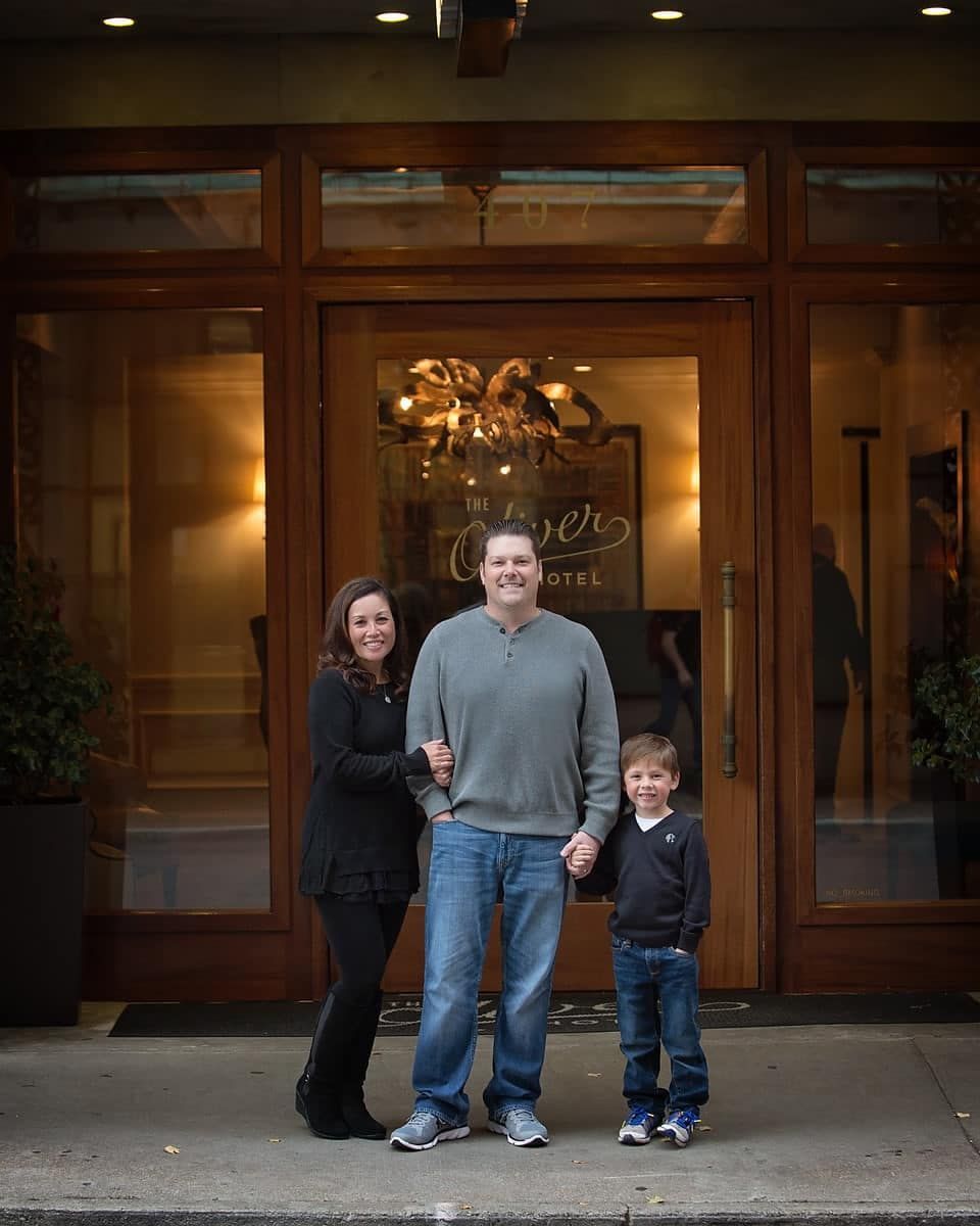 Family of three poses outside a hotel entrance; mother, father, and son smile.