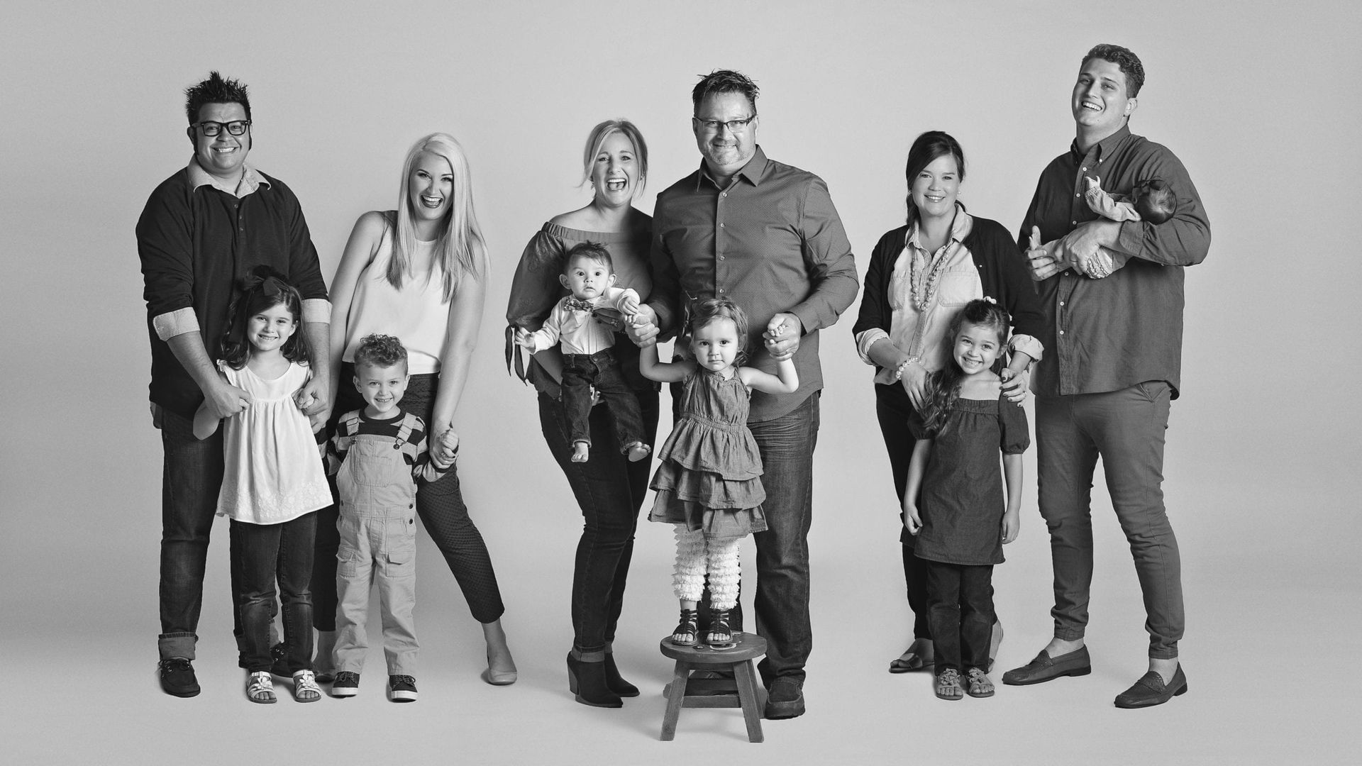 Large family group in black and white. Smiling adults and children posing in studio.