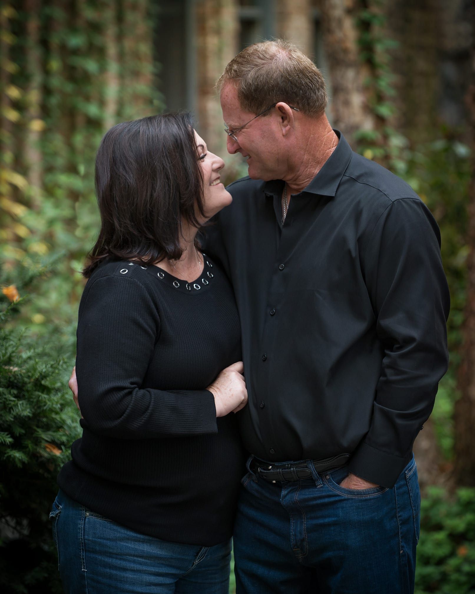 Couple smiling at each other, outdoors. Woman in black sweater, man in black shirt and jeans.