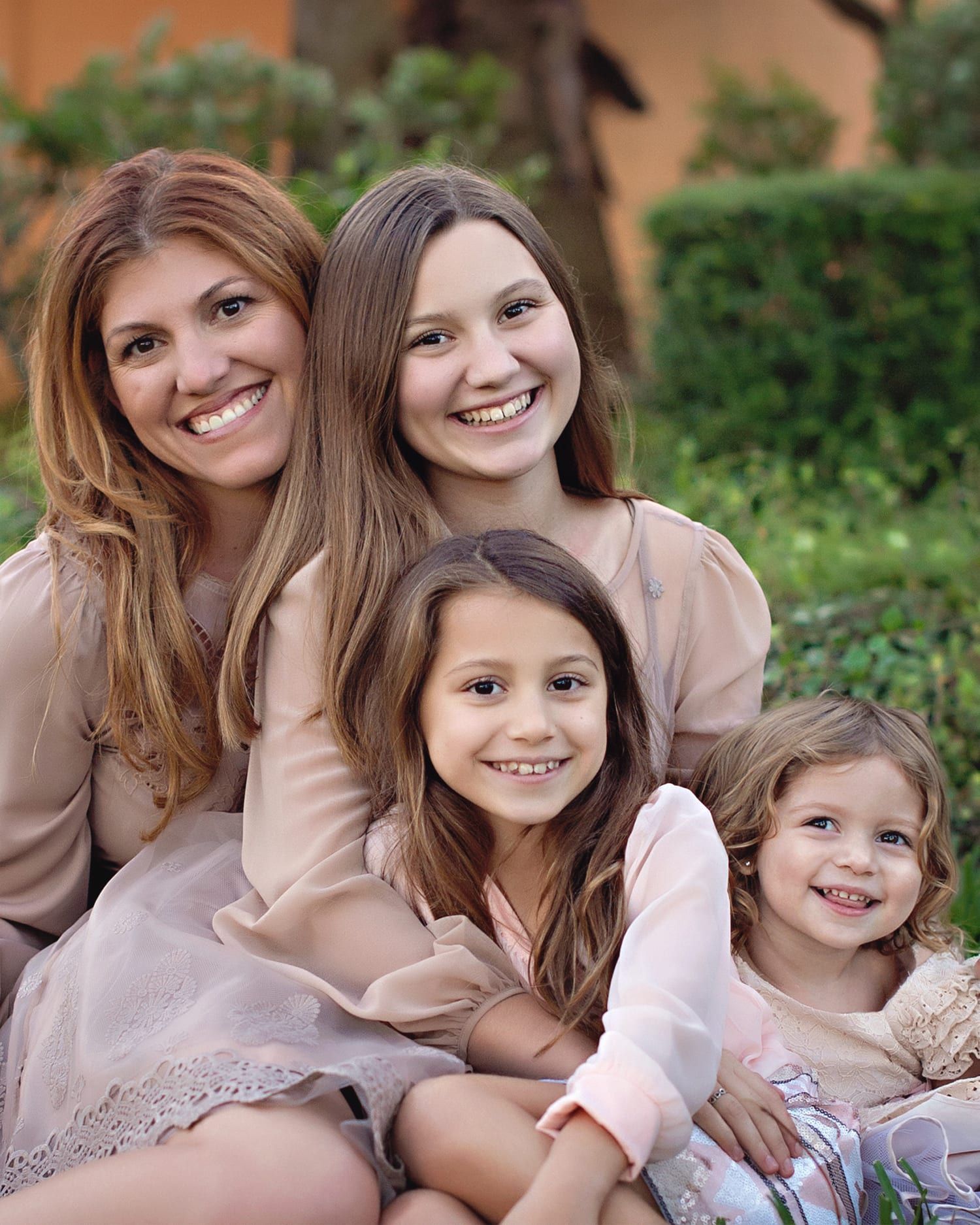 A woman and three smiling daughters pose outside; all wear beige clothing.