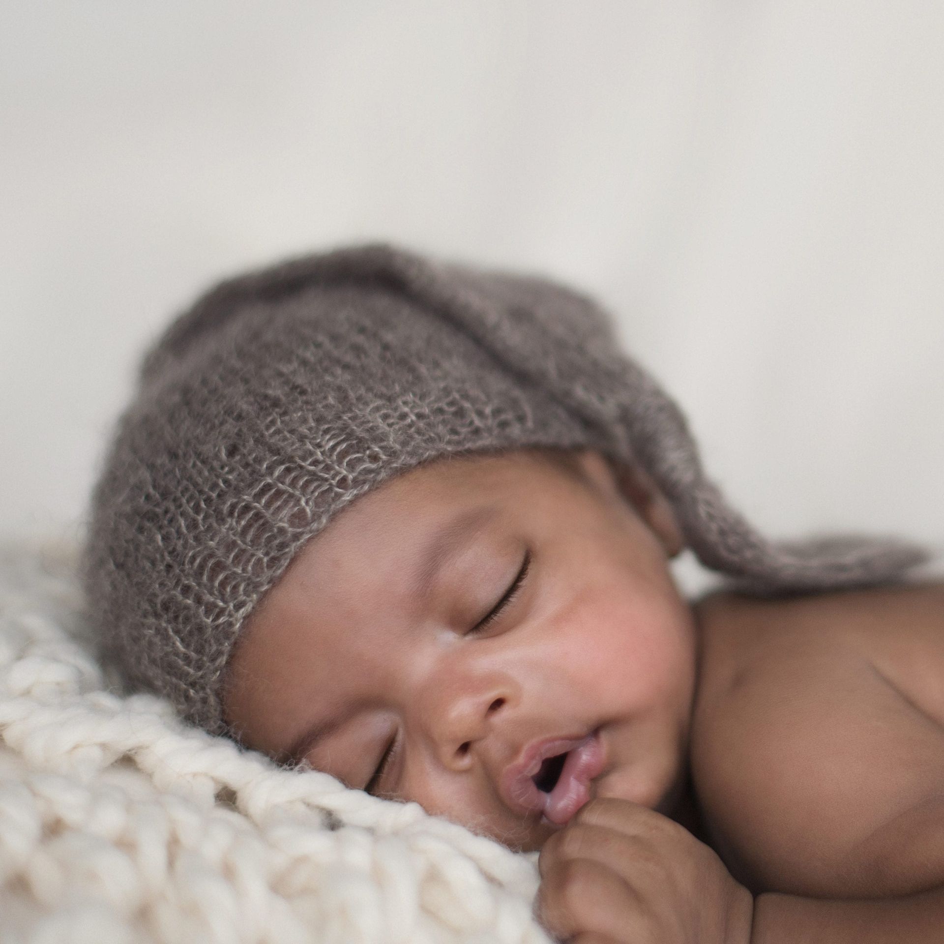 Sleeping baby wearing a brown hat, resting on a cream-colored blanket.