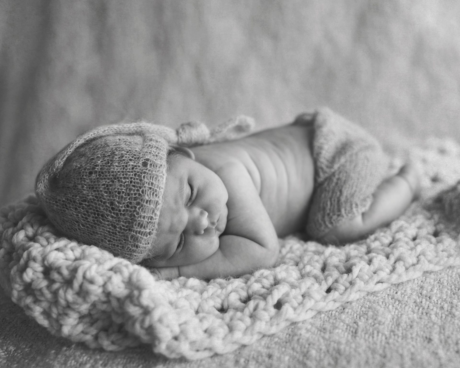 Newborn baby sleeping on a crocheted blanket, wearing a hat and diaper, in black and white.
