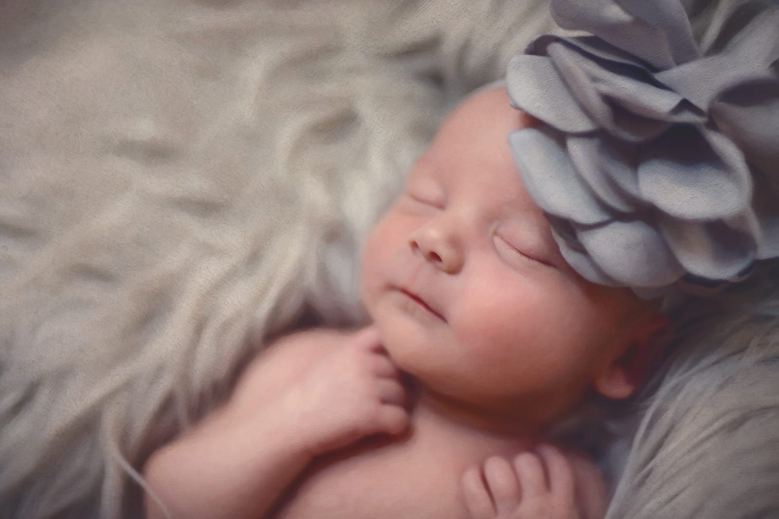 Newborn baby sleeping, wearing gray floral headband, nestled in faux fur.