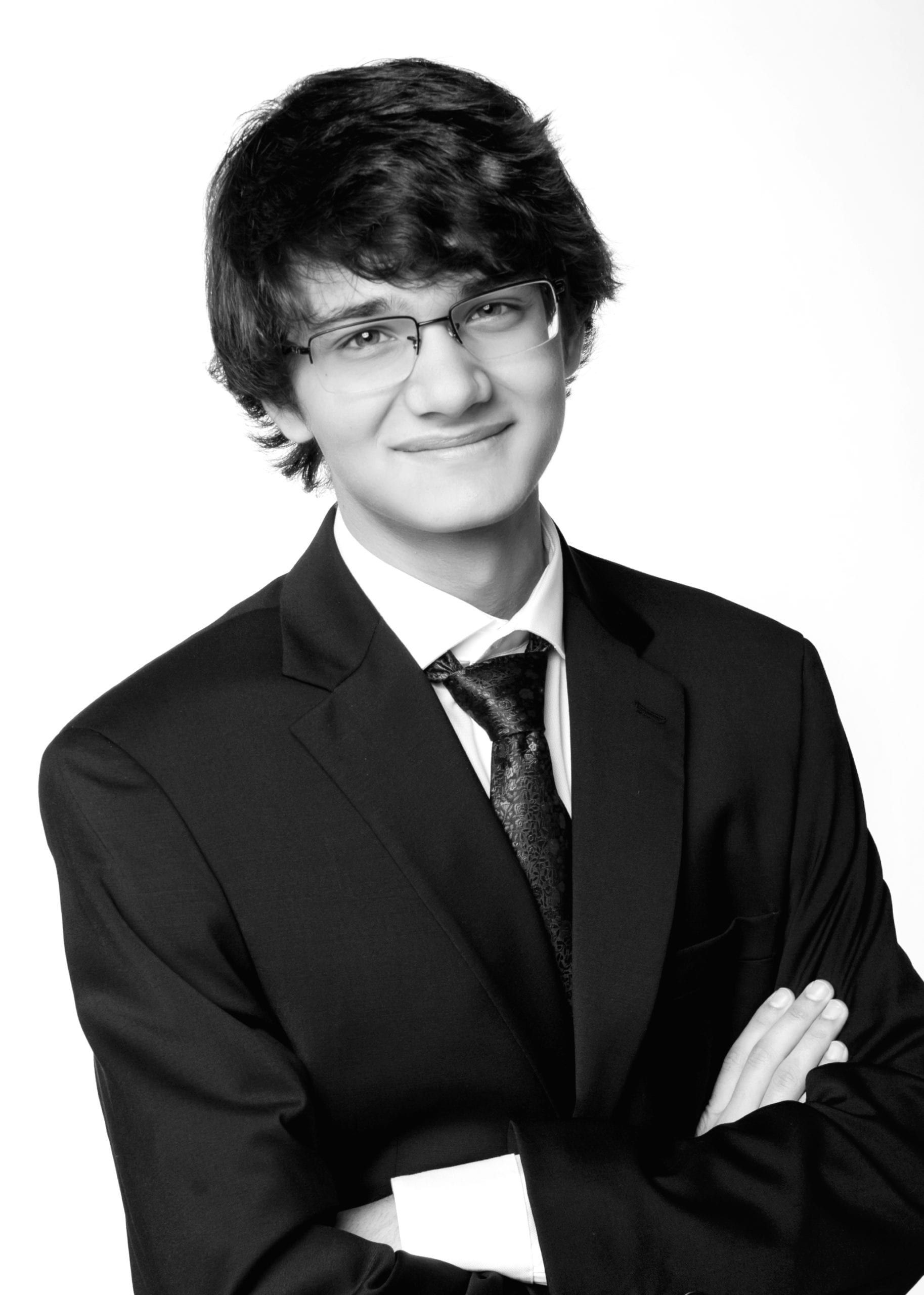 Teenager in a suit, wearing glasses, arms crossed, smiling, studio shot.
