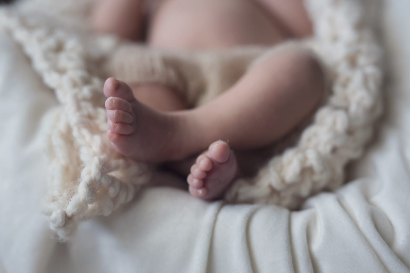 Baby's crossed feet, close-up, resting on a soft, cream-colored blanket.