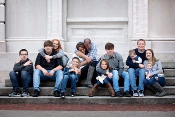 Family of eleven poses on stone steps; some are hugging.