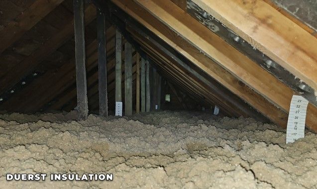 Attic space with brown insulation between wooden beams and supports.