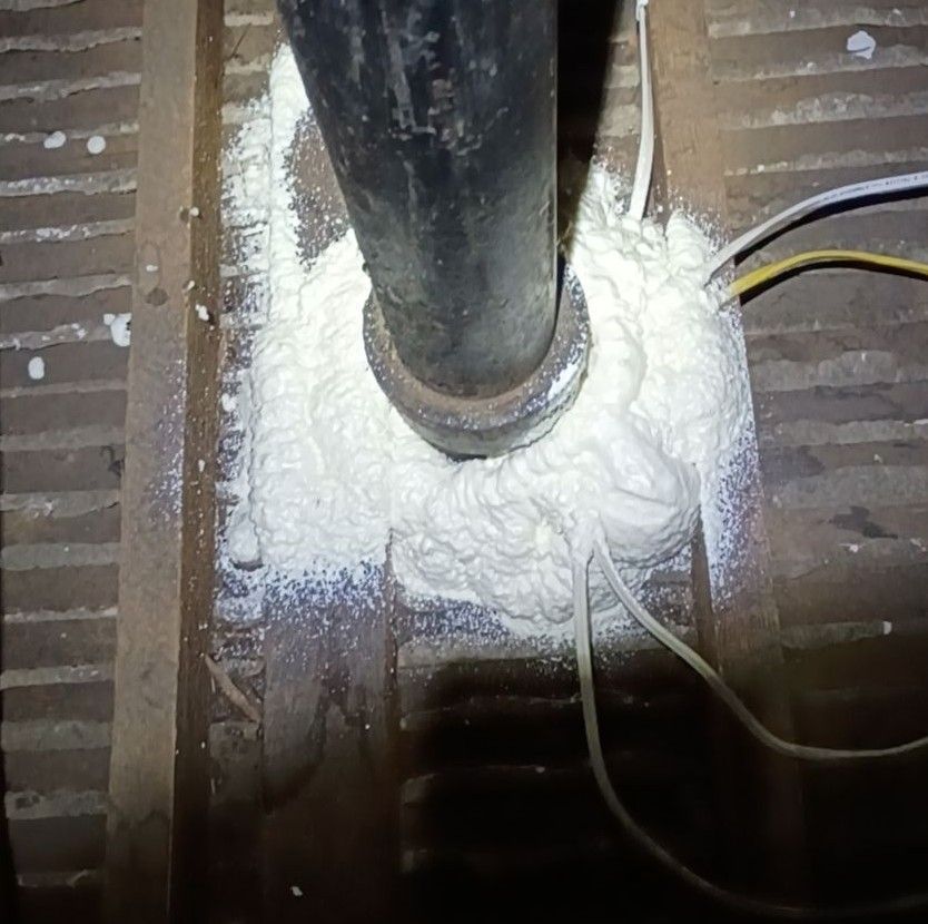 Person applying sealant to a metal duct in an attic, using a caulking gun.
