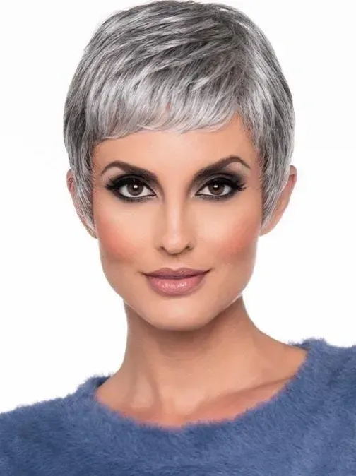 Portrait of a person with short silver hair, dramatic eye makeup, and a fuzzy blue top, smiling softly