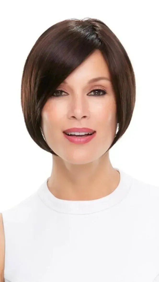 Studio portrait of a person with a dark bob haircut, wearing a white shirt and smiling on a white background