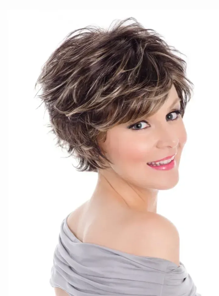 Smiling woman with short layered brown hair wearing a gray off-shoulder top on a white background