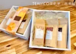 木桌上放著兩個茶葉禮盒。每個盒子裡都裝著一個用牛皮紙包裹的茶包,其中一個茶包的外包裝上有一個花紋。