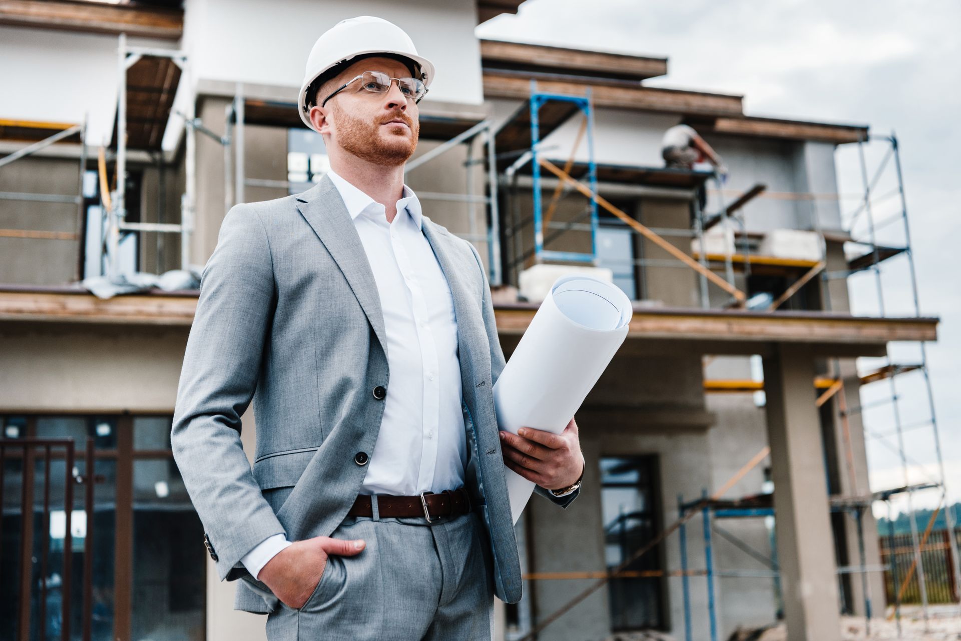 Engineer in hard hat holding blueprints at a construction site under renovation