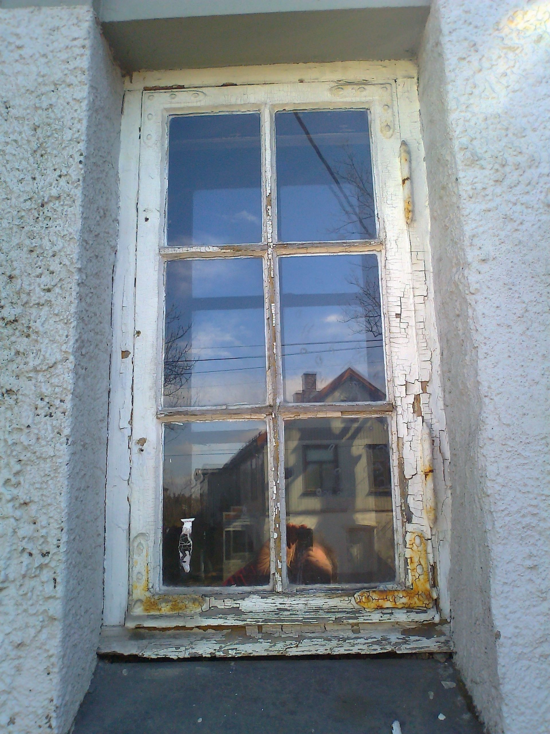 A window with peeling paint and a reflection of a building