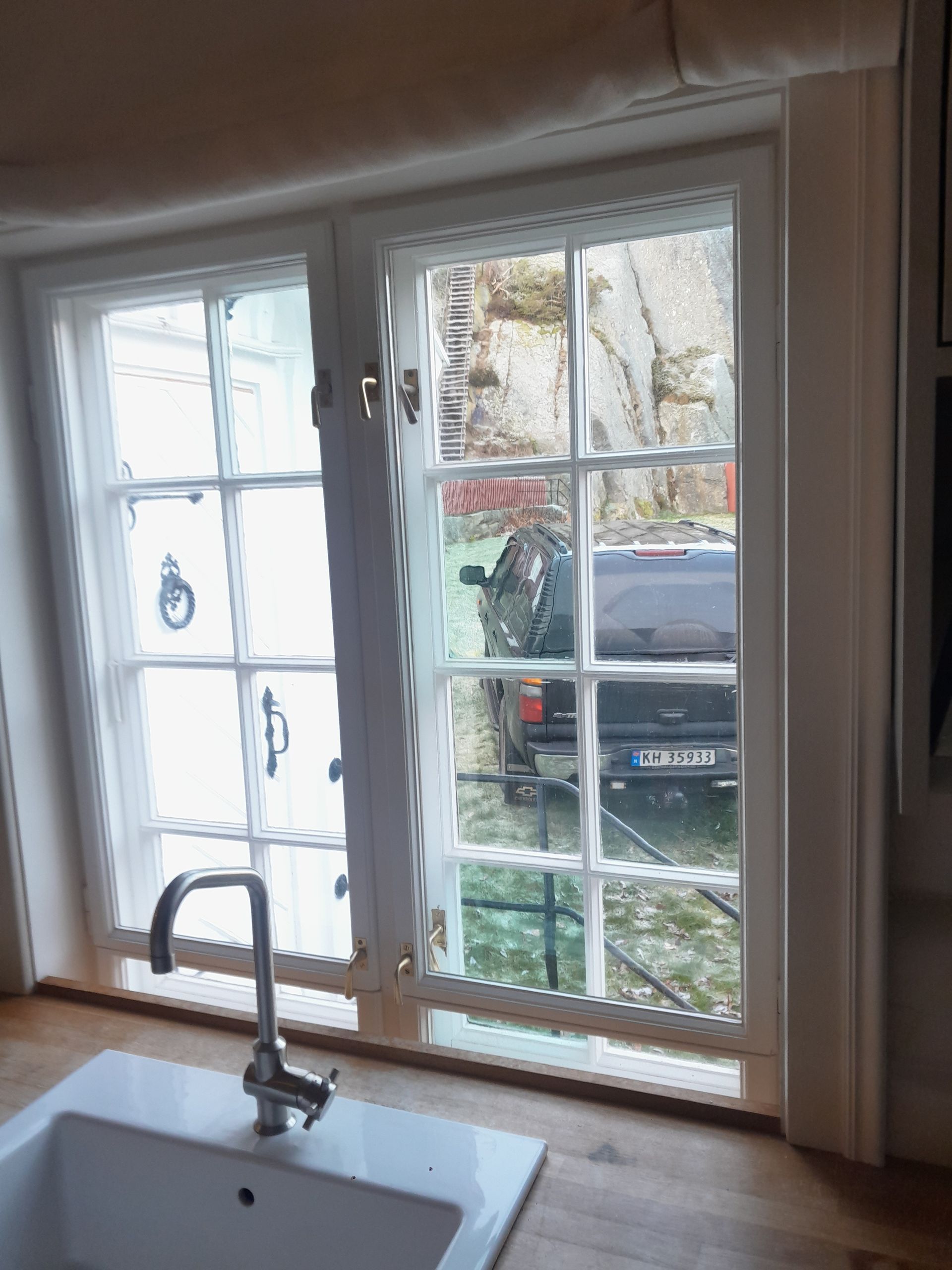 A kitchen with a sink and a window with a car in the background.