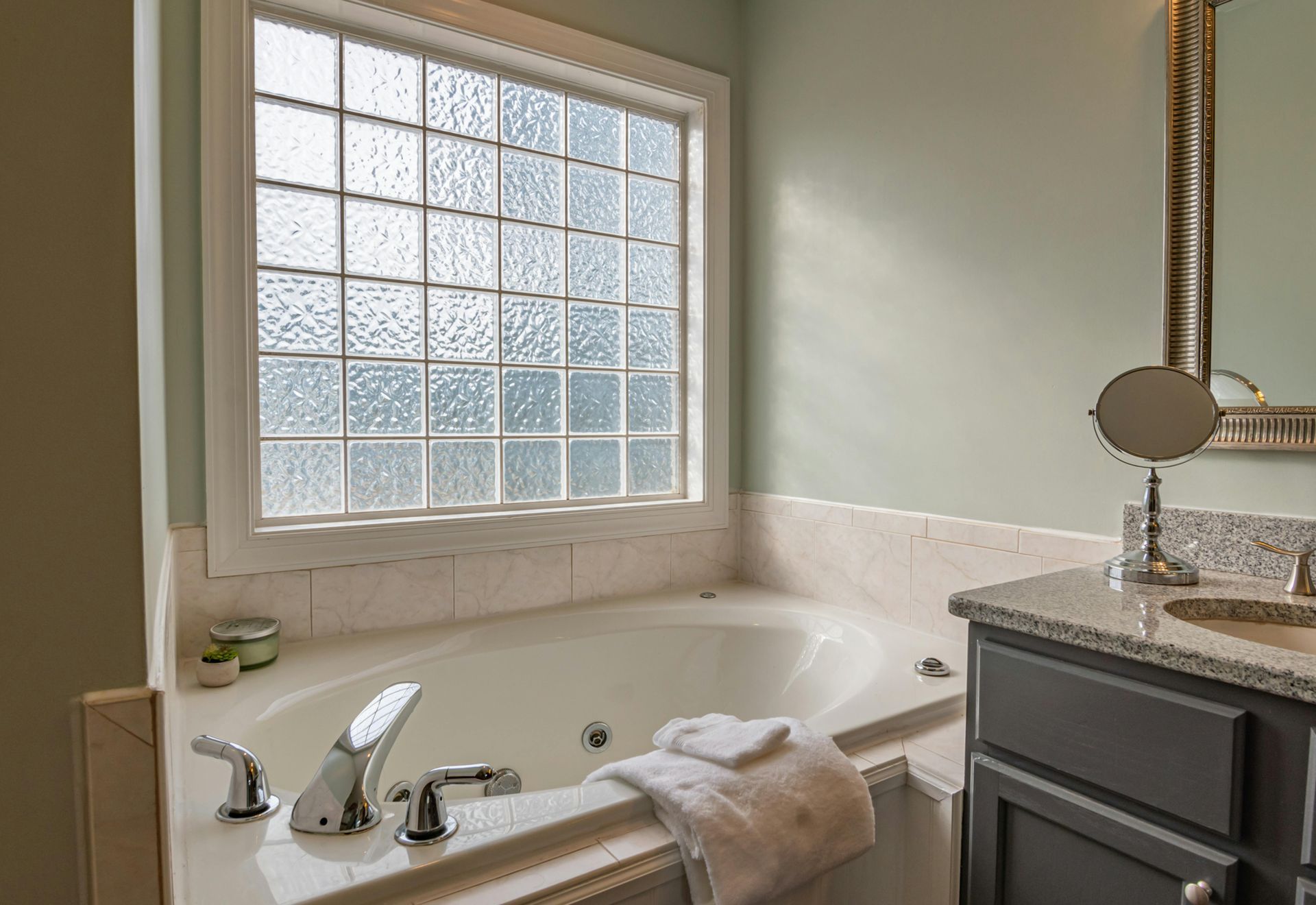 Bathroom with a white bathtub under a frosted window, with a vanity and mirror on the right side.