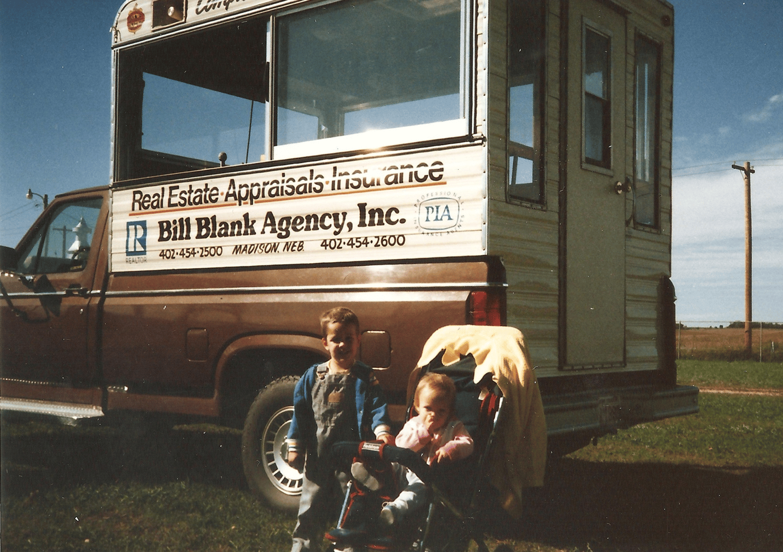 Two children in front of a brown truck with a boxy office on the back; advertising real estate services.
